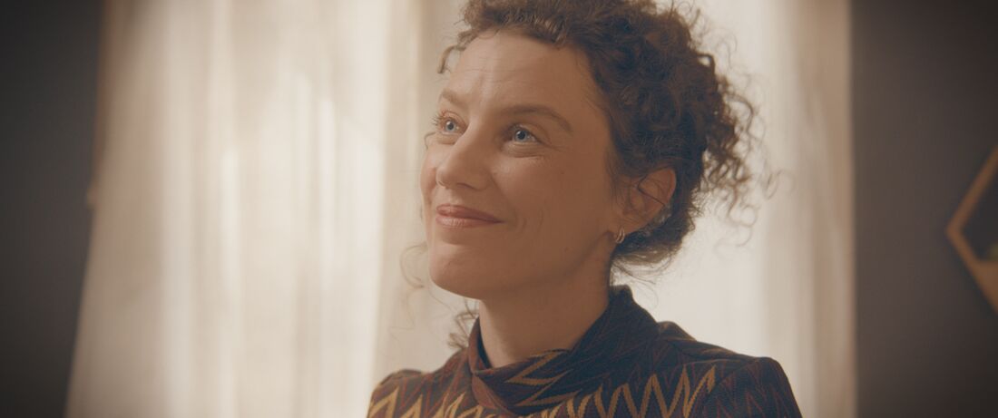 Portrait d’une femme souriante devant un rideau baigné de lumière