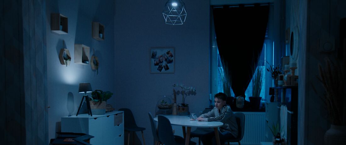 Un enfant assis seul à la table d’un séjour plongé dans la lumière bleue de la nuit